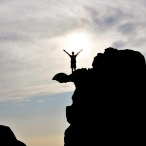 Silhouette of a person celebrating on a mountain peak against a dramatic sky, symbolizing freedom and success.